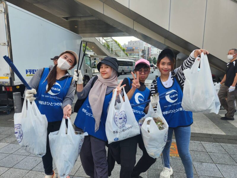 4人（女性3人、男性1人）がゴミ袋を持ってポーズをとっている